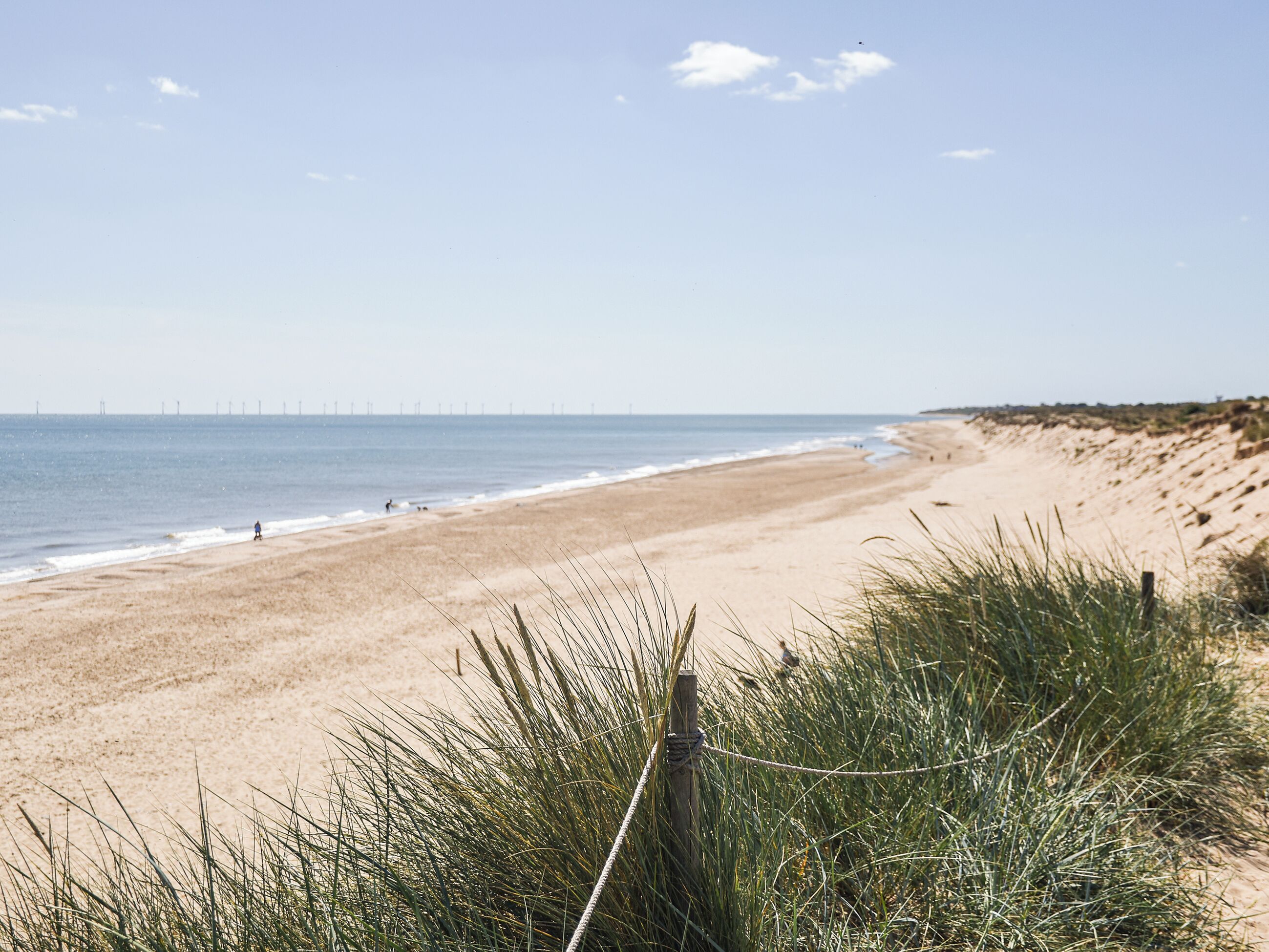 A beach with a fence in the foreground and a distant view of wind turbines.