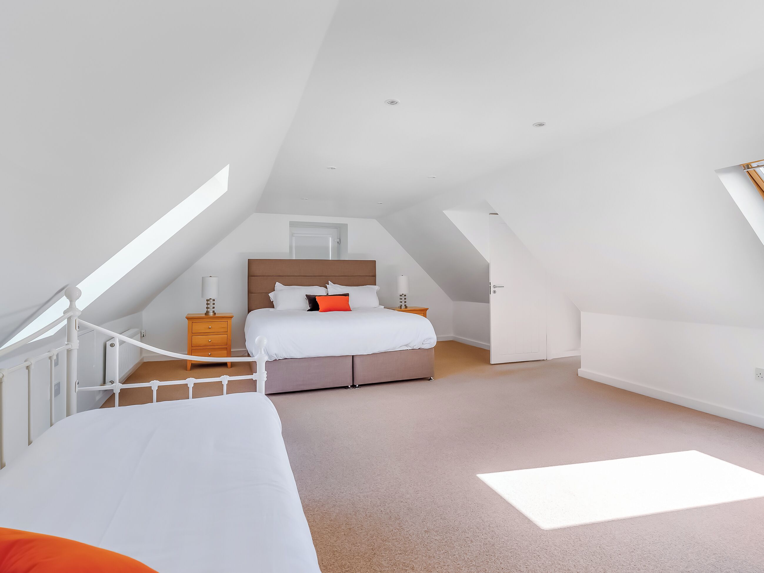 Een slaapkamer met schuine wand, een bed met wit beddengoed, een nachtkastje en een dressoir.