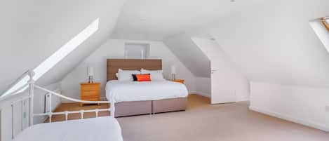 Een slaapkamer met schuine wand, een bed met wit beddengoed, een nachtkastje en een dressoir.