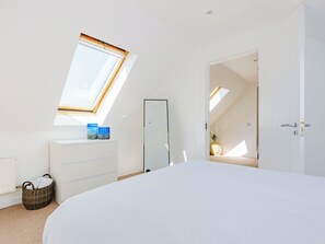 Ein Schlafzimmer mit Oberlicht, einem Bett, einer Kommode und einer Tür zu einem weiteren Raum.
