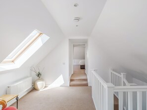 Ein Zimmer mit schrägem Dach, einem Oberlicht, einer Heizung, einer weißen Heizung, einer weißen Wand, einer weißen Treppe und einem weißen Geländer.