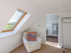 A room with a skylight, a white chair with colorful cushions, and a view of a bathroom. - The Stables - UK52287 (Auchincruive)