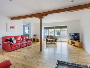 Ein Wohnzimmer mit einem roten Ledersofa, einem karierten Sessel, einem Holztisch und einem Fernseher auf einem Holzschrank.