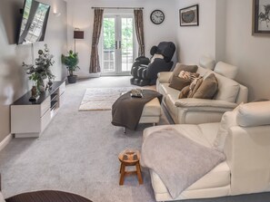 A modern living room with a sofa, a coffee table, a small stool, a television, and a window with curtains. - 3 bedroom accommodation in Fleggburgh (Fleggburgh)