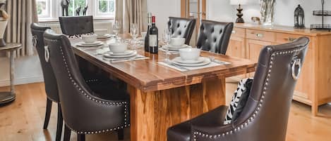 Een eetkamer met een houten tafel voor vier personen, omringd door lederen stoelen, een kast en een vaas met bloemen.