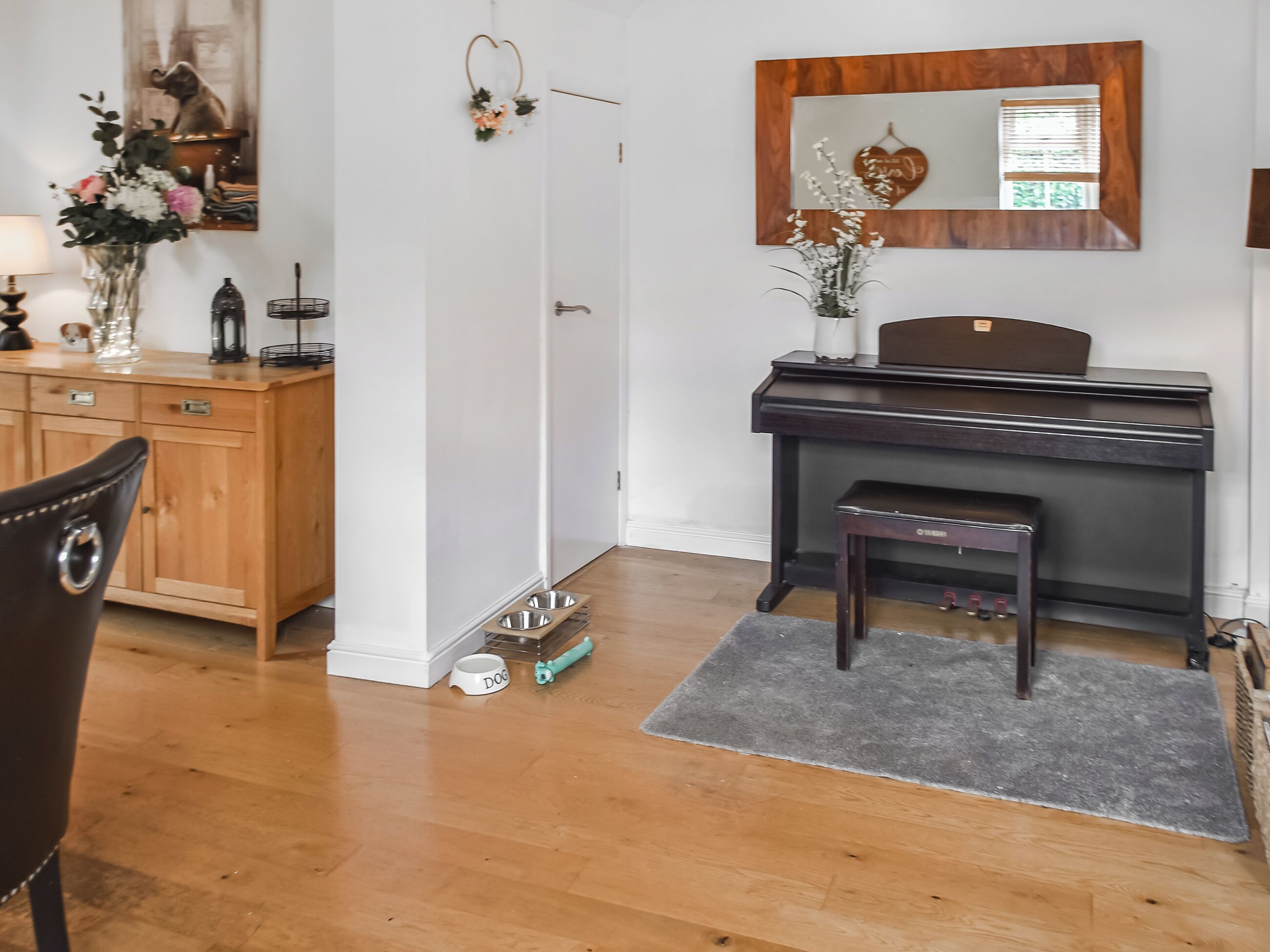 A room with a wooden desk, a piano, a dog bowl, and a small bench.