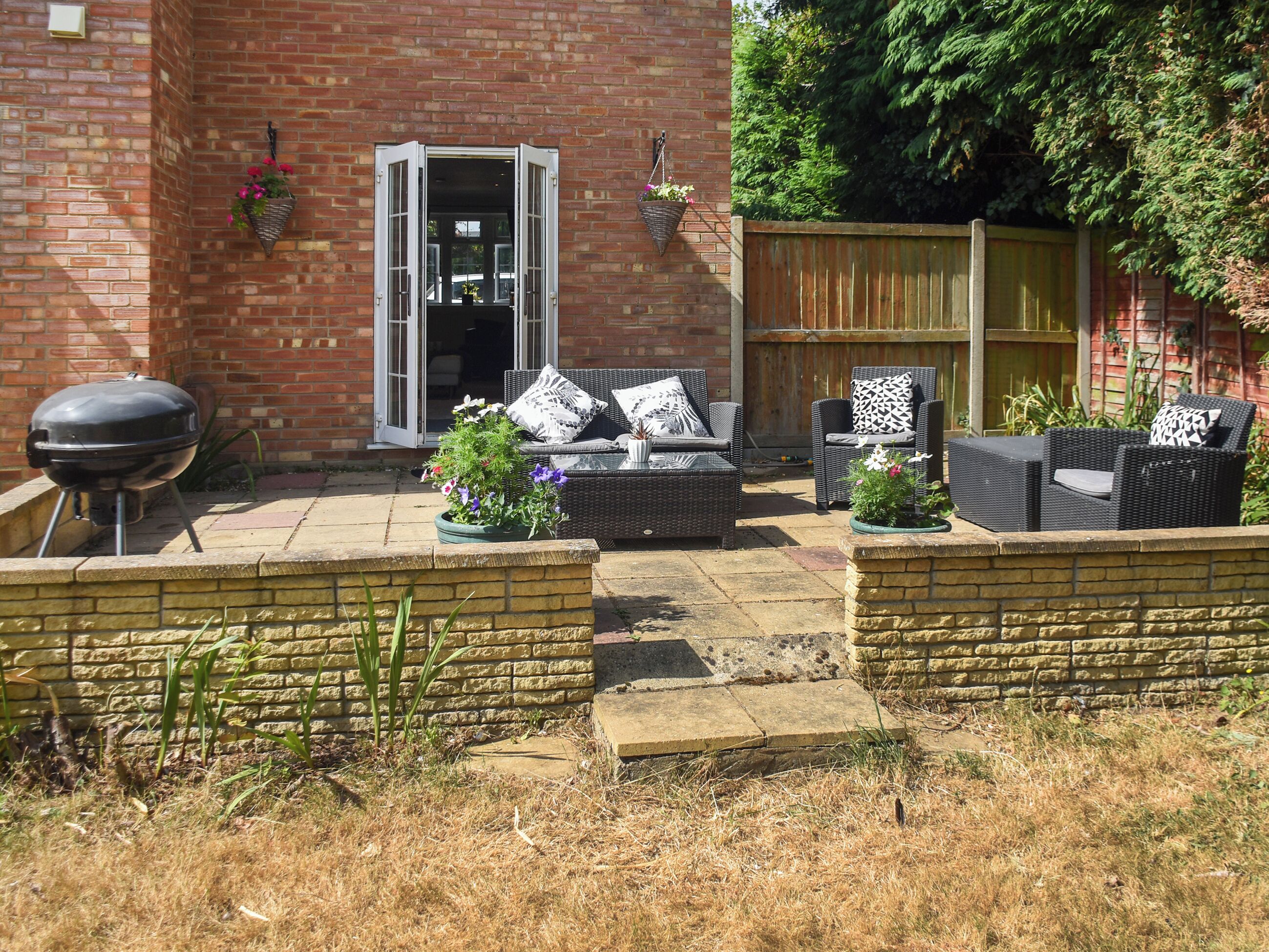 A patio area with outdoor furniture, a barbecue grill, and a brick wall.
