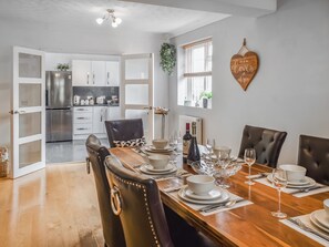 A dining area with a wooden table set for six, surrounded by leather chairs. A kitchen is visible in the background with white cabinets and stainless steel appliances. - 3 bedroom accommodation in Fleggburgh (Fleggburgh)
