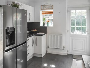 A modern kitchen with stainless steel appliances, white cabinetry, a small window with a view, and a door with a white panel. - 3 bedroom accommodation in Fleggburgh (Fleggburgh)