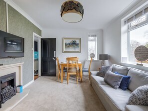 Ein Wohnzimmer mit Kamin, Fernseher, Esstisch mit Stühlen, einer Couch und einem Fenster mit Blick.