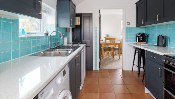 A compact kitchen with a washing machine, a sink, and a dining area with chairs. - The Paddock - UK52288 (Auchincruive)