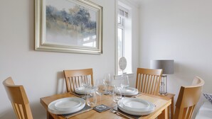 A dining table set with plates, glasses, and cutlery, surrounded by wooden chairs, with a framed painting on the wall. - The Paddock - UK52288 (Auchincruive)