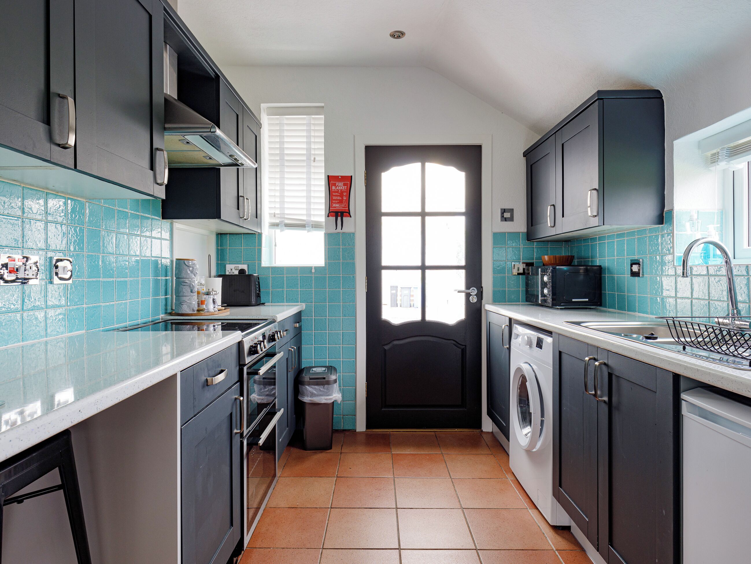 A kitchen with a tiled backsplash, stainless steel appliances, and a window with blinds.