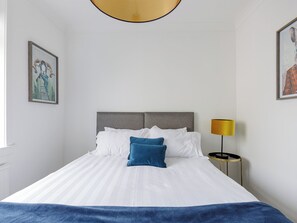 Ein Hotelzimmer mit einem Bett, einer Nachttischlampe und zwei gerahmten Kunstwerken an den Wänden.