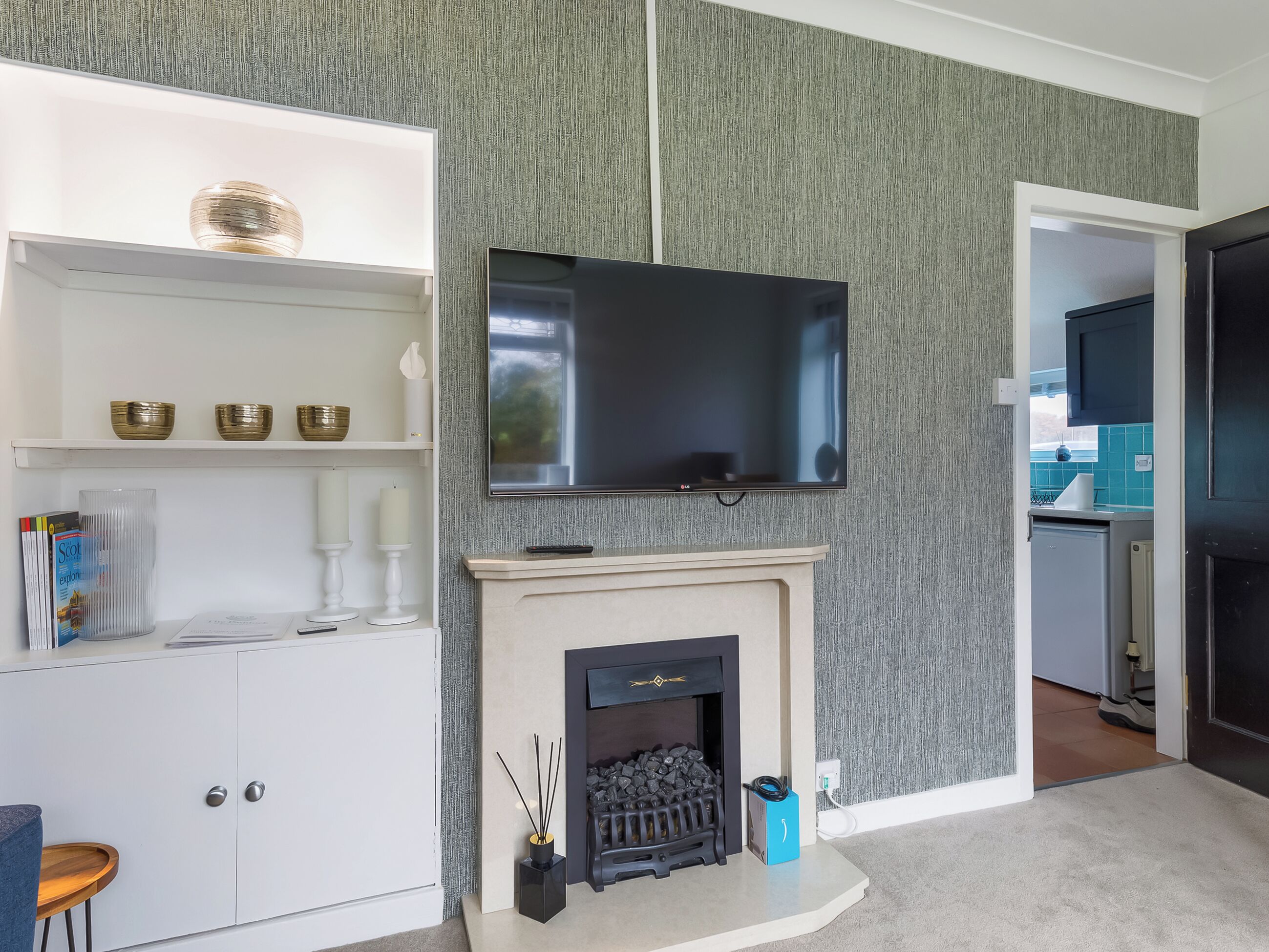 A modern living room with a fireplace, a flat-screen TV mounted on the wall, and a white entertainment unit with decorative items.