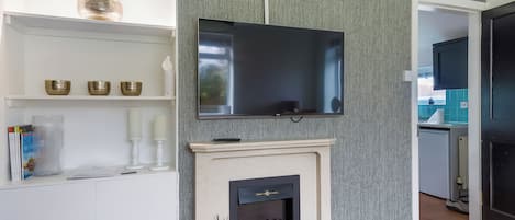 A modern living room with a fireplace, a flat-screen TV mounted on the wall, and a white entertainment unit with decorative items.