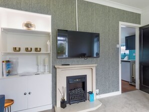 Ein modernes Wohnzimmer mit Kamin, einem an der Wand befestigten Flachbildfernseher und einer weißen Unterhaltungsanlage mit Dekorationselementen.