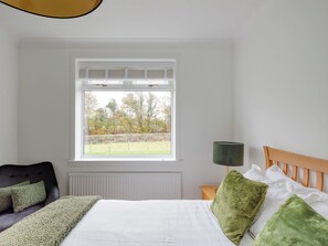 Une chambre à coucher avec un lit, une fenêtre donnant sur des arbres, une table de chevet avec une lampe et une tête de lit.