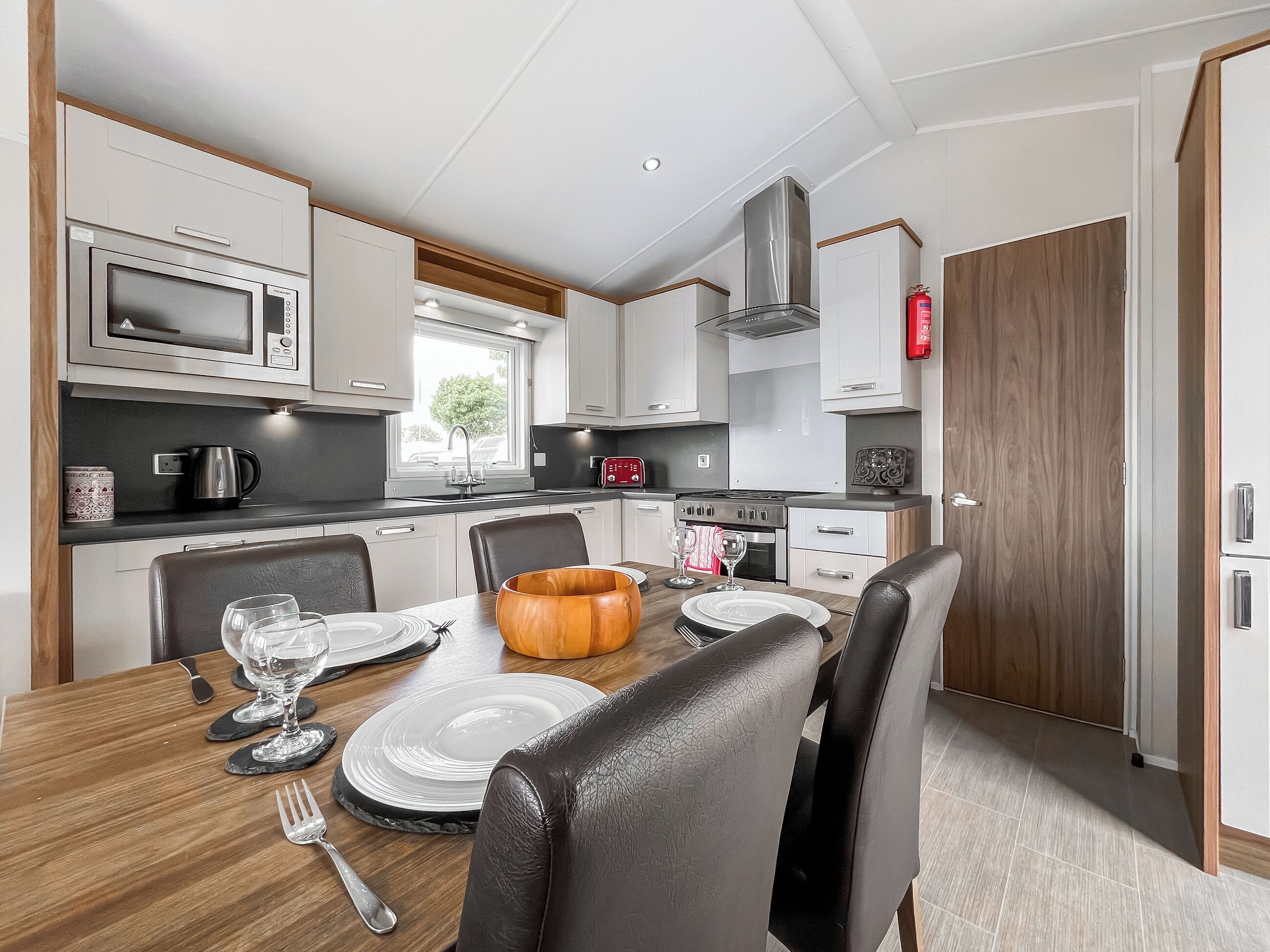 A modern kitchen with white cabinetry, a microwave, a stove, and a dining area with a wooden table set for two.