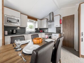 Una cocina moderna con armarios blancos, microondas, estufa y un comedor con una mesa de madera para dos personas.