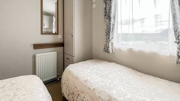 A bedroom with two beds, a wardrobe, a mirror, and a window with curtains.