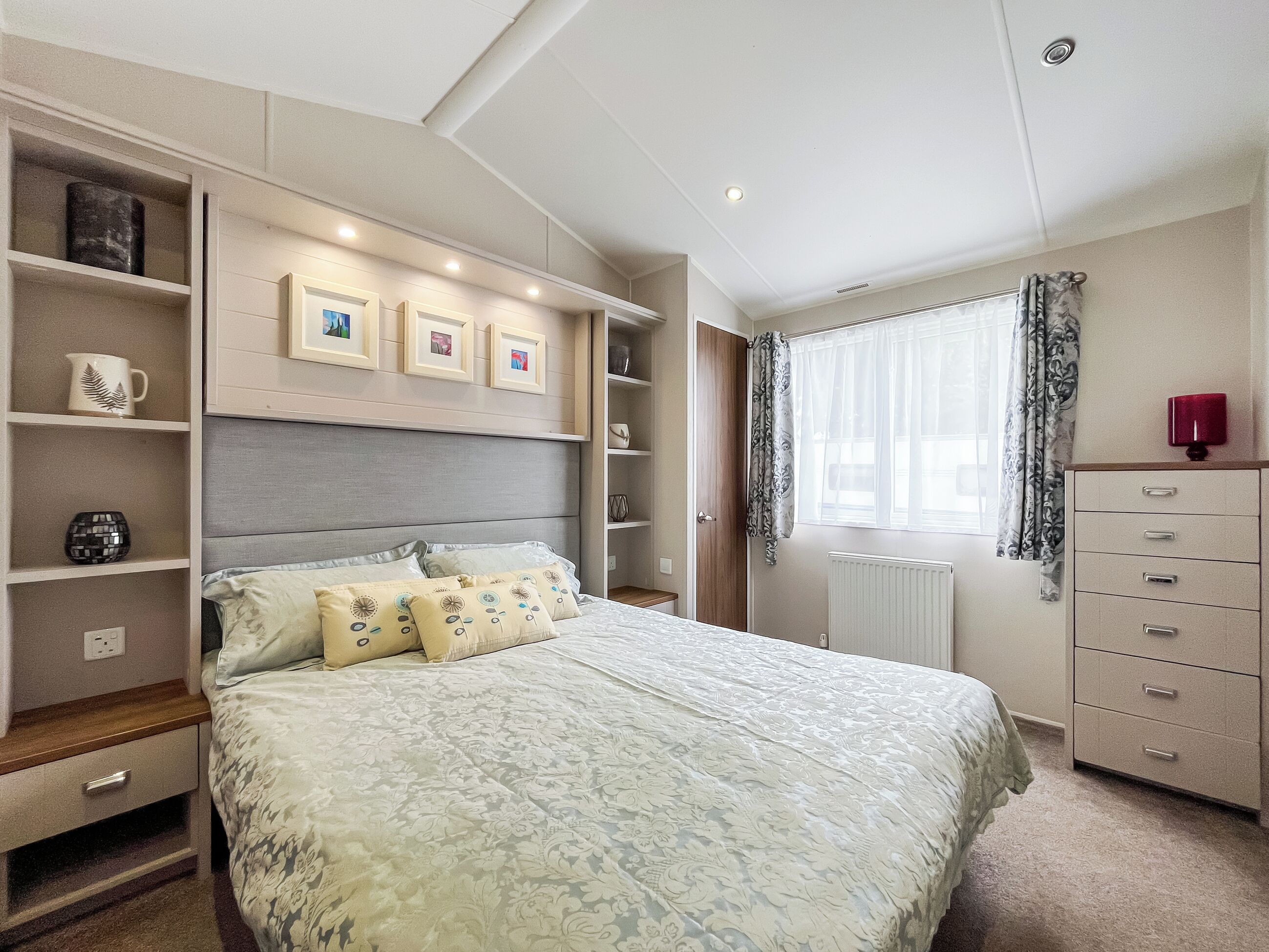 A bedroom with a bed, built-in shelving, a dresser, and a window with curtains.