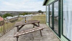 Una terraza de madera con una mesa de picnic y una botella de vino, con vista a un parque de caravanas.
