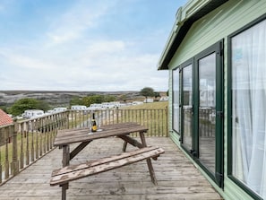 Um deck de madeira com uma mesa de piquenique e uma garrafa de vinho, com vista para um parque de caravanas.