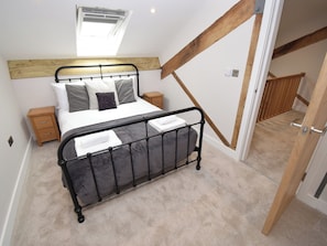 A bedroom with a bed, bedside tables, a wooden headboard, a skylight, and a staircase. - 6 bedroom accommodation in Carnforth (Carnforth)