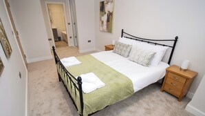 A neatly made bed with a green bedspread and white linens, a wooden nightstand with a lamp, and a painting on the wall. - 6 bedroom accommodation in Carnforth (Carnforth)