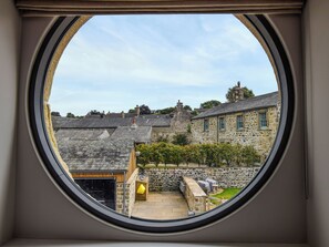 A view through a window of a stone building with a stone wall, a wooden deck, and a small garden area. - 6 bedroom accommodation in Carnforth (Carnforth)