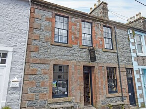 A two-story stone building with a traditional design, featuring a visible entrance and a signboard above the door.