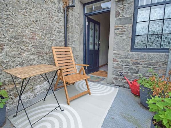 A wooden chair and table set on a patterned rug outside a stone building with a blue door.