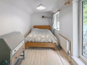 A narrow room with a bed, a dresser, a radiator, and a window.