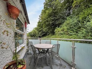 An outdoor patio with a round table and chairs, a potted plant, and a view of a green hillside.