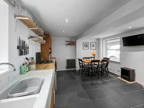 A modern kitchen with a dining area, a built-in stove, and a TV mounted on the wall. - 2 bedroom accommodation in Plympton (Plympton)