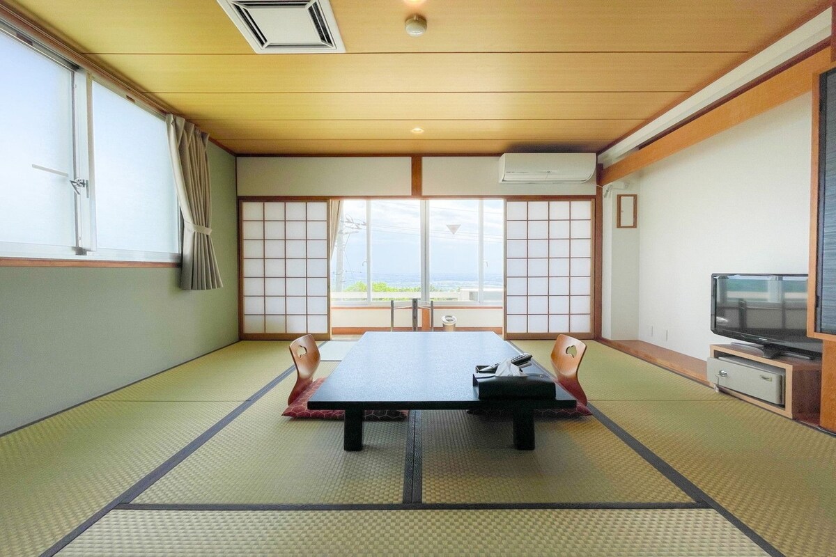 A traditional Japanese-style room with tatami flooring, a low table, a television, and a sliding door with a view.