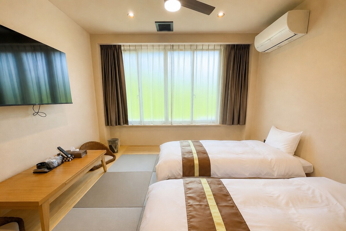 A hotel room with two beds, a desk, a chair, a television, and an air conditioning unit.