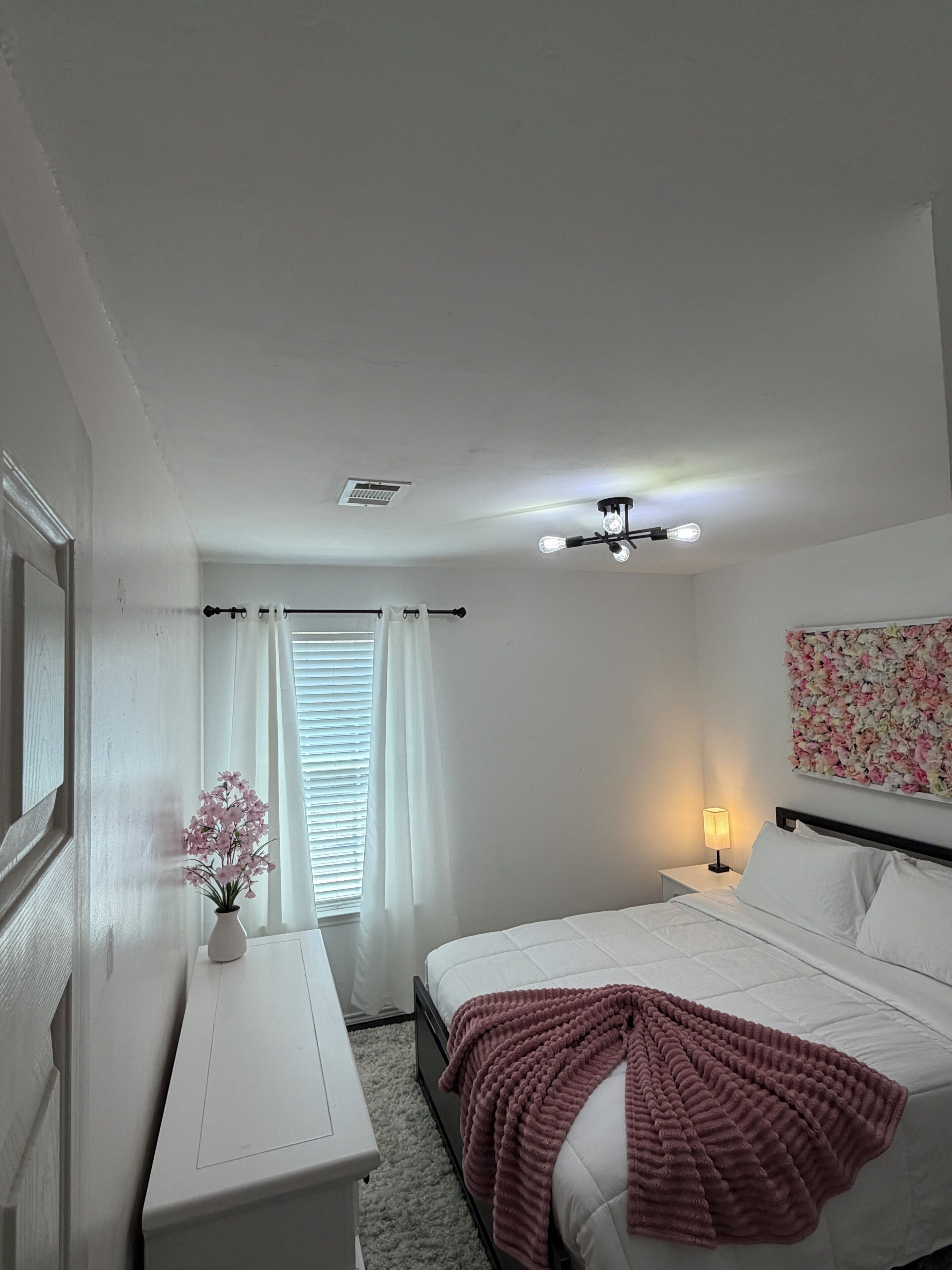 A bedroom with a bed, bedside table, lamp, and a wall-mounted floral artwork.
