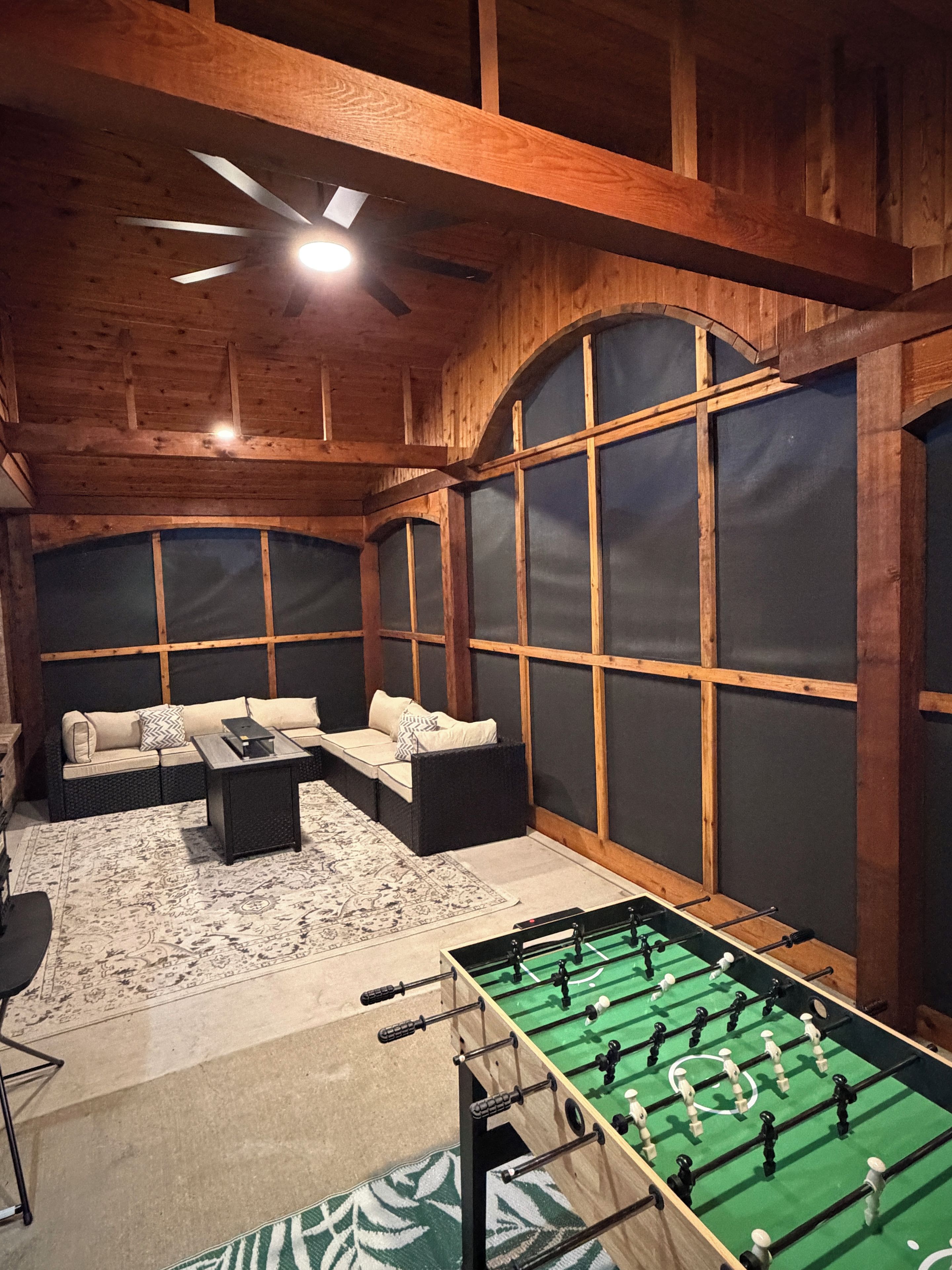 A room with a sofa set, a foosball table, and a patterned rug.
