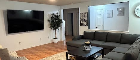 A living room with a flat-screen TV, a ceiling fan, a dark-colored sofa, a coffee table, and a patterned rug.