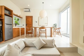 Uma cozinha moderna com geladeira, armários e uma janela com plantas. Há uma área de jantar com mesa, cadeiras e um lustre.