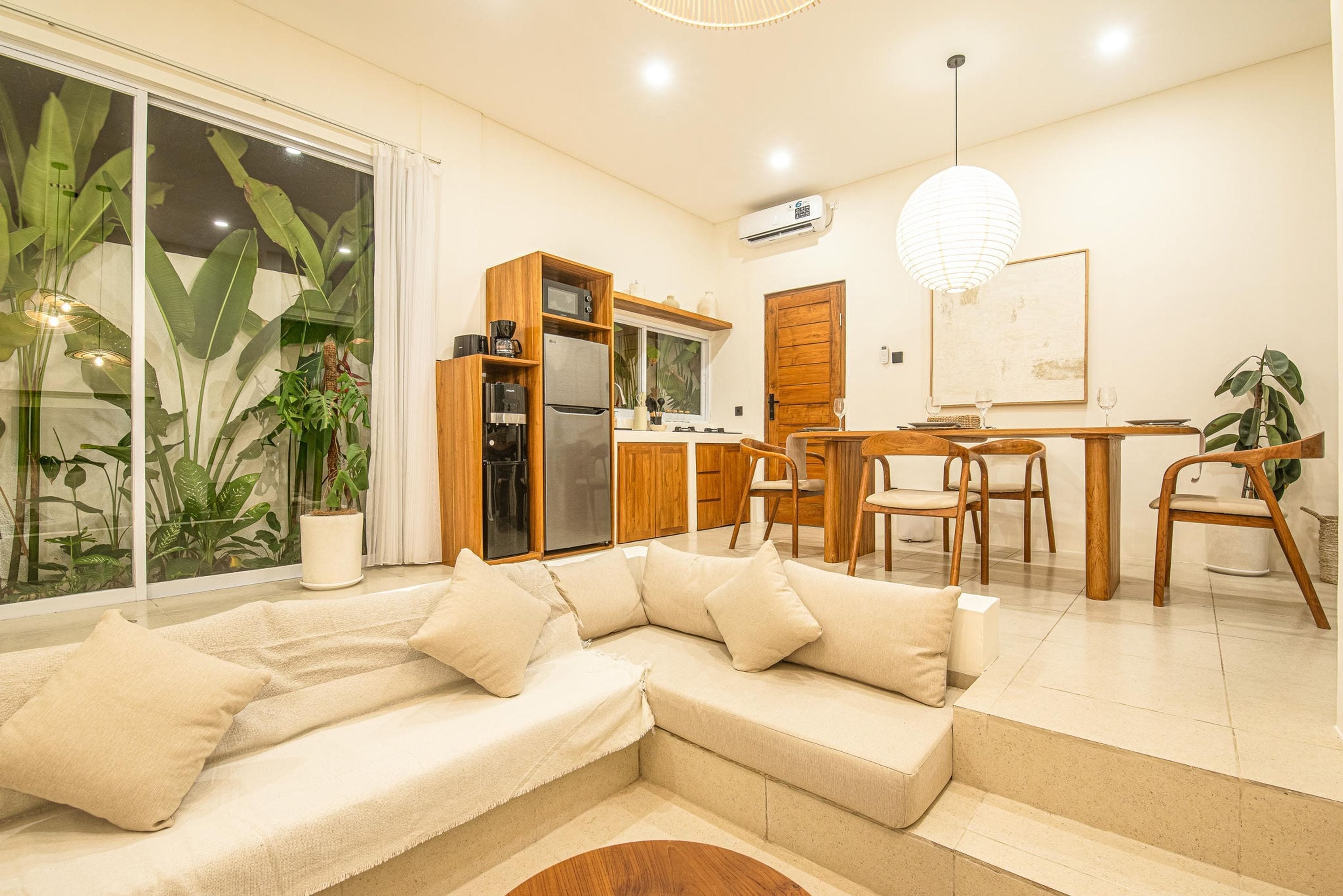 Uma sala de estar moderna com um sofá seccional, uma área de jantar com mobiliário de madeira e uma cozinha com forno embutido e micro-ondas.