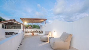 Eine Dachterrasse mit überdachter Sitzgelegenheit, einem Esstisch und Blick auf die umliegende Landschaft.