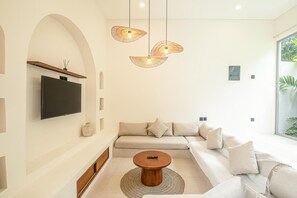 A modern living room with a sofa, a coffee table, and a flat-screen TV mounted on the wall. - Brand New 2br Uluwatu Villa 2 Mins to Beach (Pecatu)