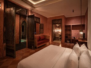 Une chambre spacieuse avec un grand lit, une armoire en bois, un canapé rouge et une salle de bain visible à travers une porte ouverte.