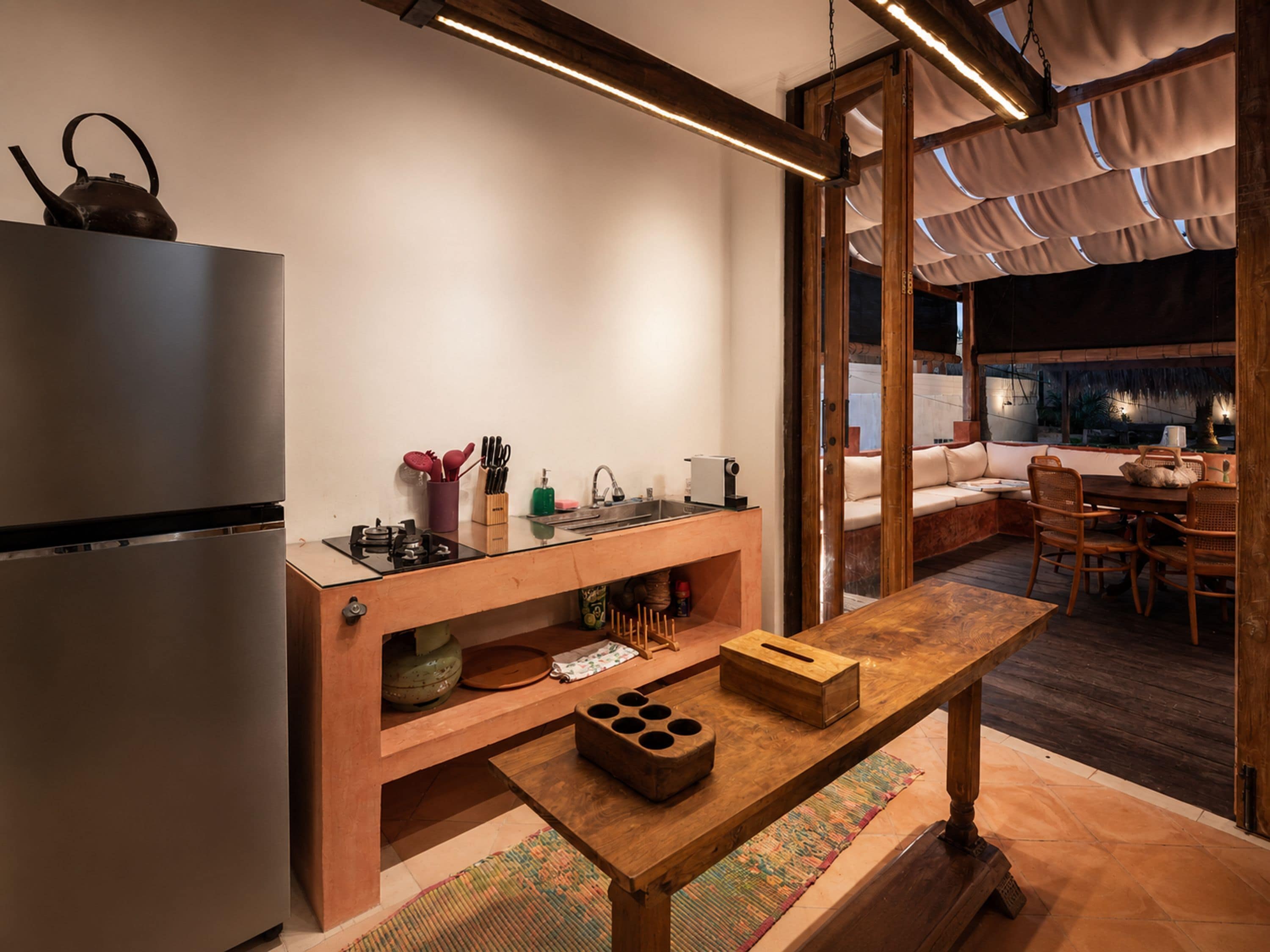 Una cucina moderna con frigorifero integrato, tavolo in legno e vista sull'area salotto esterna.
