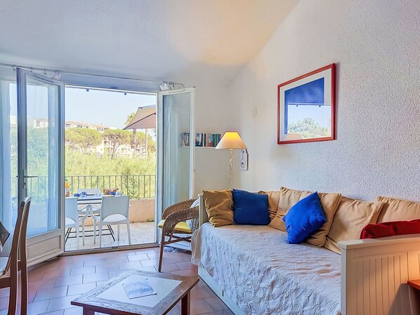 Une pièce comprenant un canapé, une table, une chaise, une lampe et une porte vitrée donnant sur un espace extérieur aménagé avec une table et des chaises.