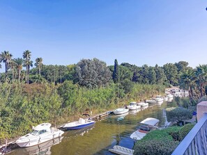 Un canal bordé de bateaux amarrés le long des rives, entouré d’une végétation luxuriante et de palmiers.