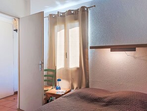 A bedroom with a bed, a chair, a table, and a window with curtains. - L'Annonciade by Interhome (Port Cogolin)